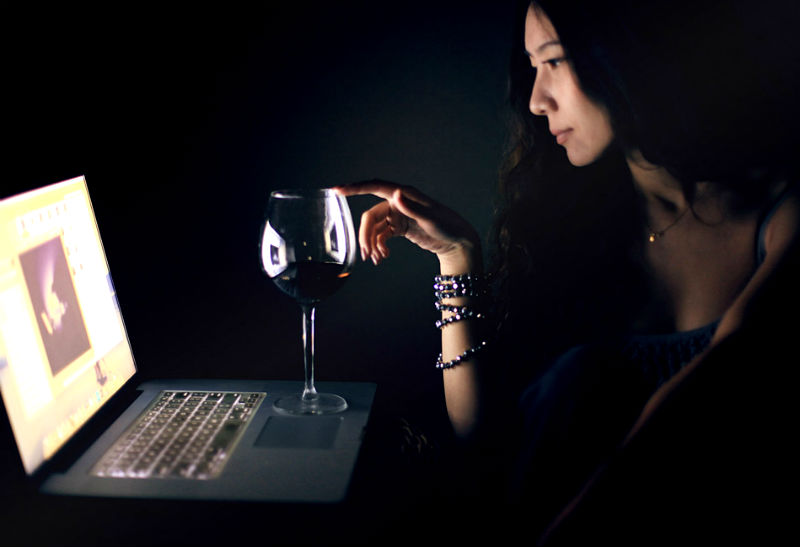 パソコンを見ながらワインを飲む女性